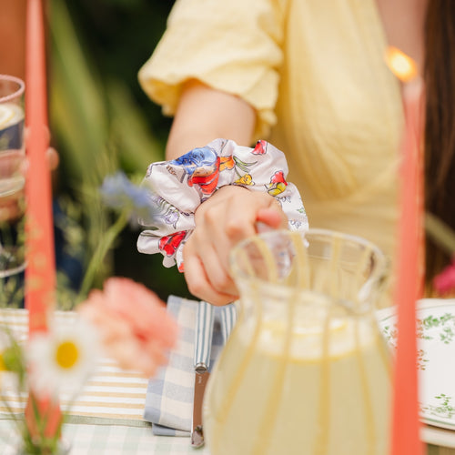 Person wearing a floral paddington bear scrunchie with a blurred background of a table setting.