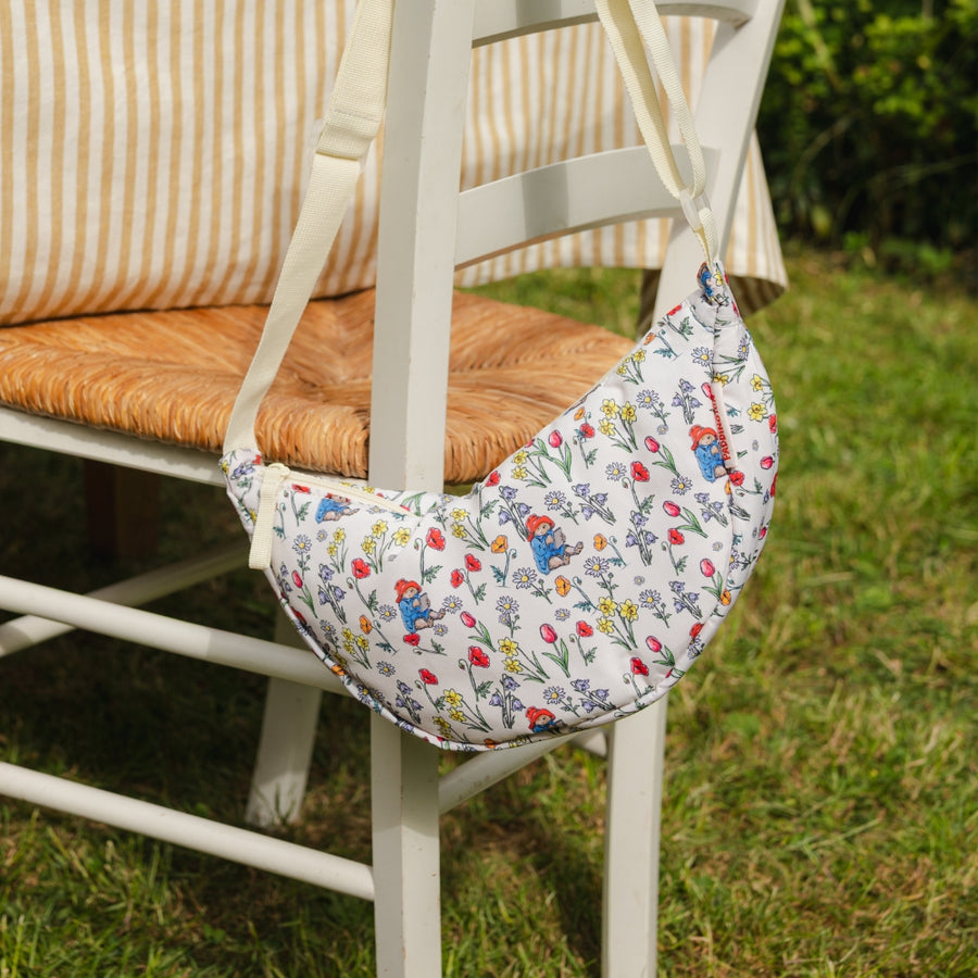 Floral-patterned crossbody Paddington bear bag attached to a chair outdoors on grass