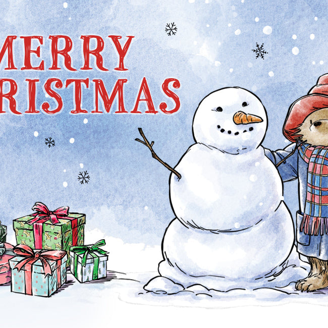 Paddington bear in the snow with a snowman next to some christmas presents and text that reads 'MERRY CHRISTMAS'