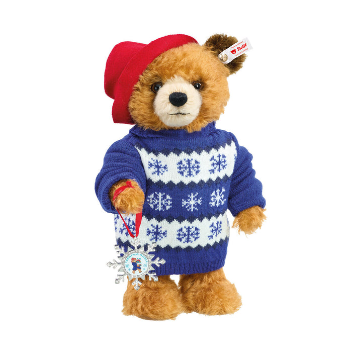 Teddy bear wearing a blue sweater with white snowflake patterns and a red hat on a white background