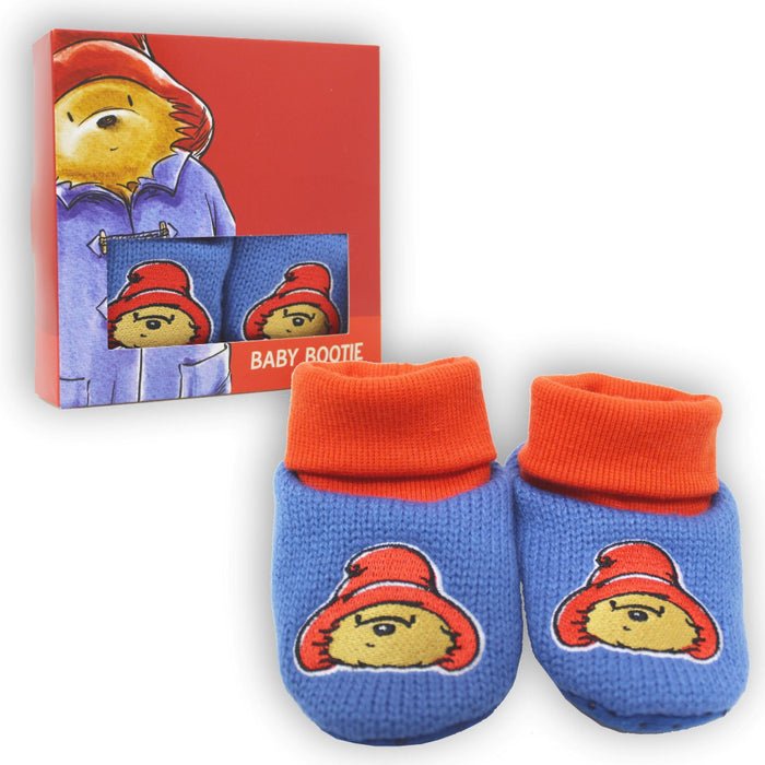 Baby booties with red cuffs and Paddington Bear design, next to packaging box.