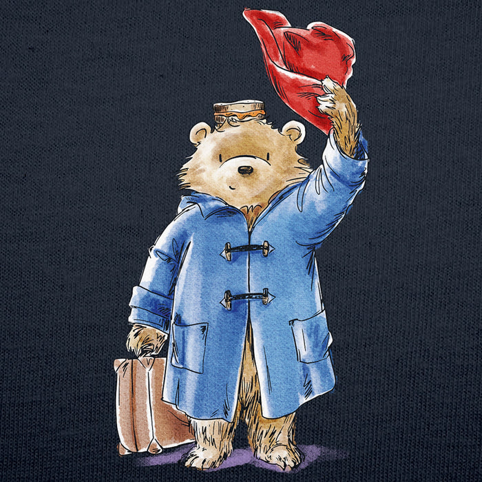A watercolor-style illustration of a teddy bear Paddington wearing a blue duffel coat and holding a red hat above its head, with a brown suitcase in one paw, set against a dark navy background.
