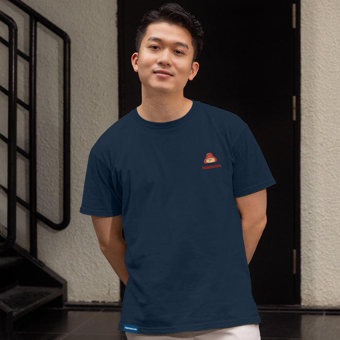An Asian man wearing a navy blue Paddington t short with logo in front of a door and set of stairs 