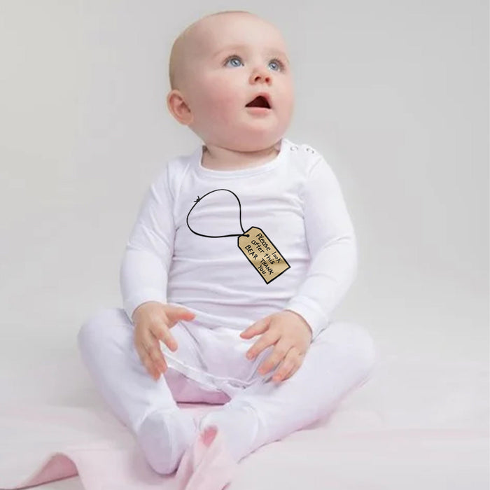Baby wearing a white onesie romper with a gold tag and text on a light gray background