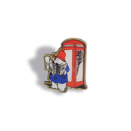 Classic paddington pin badge with phone box and reading a newspaper on a white background