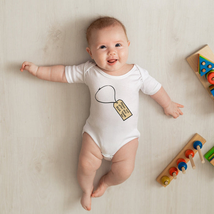 Baby wearing a white onesie with a graphic design, surrounded by colorful wooden toys on a light surface.