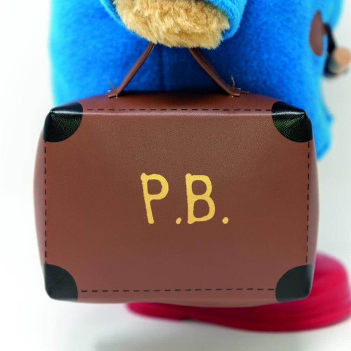 Small brown suitcase with 'P.B.' on it, held by a blue plush Paddington bear toy.