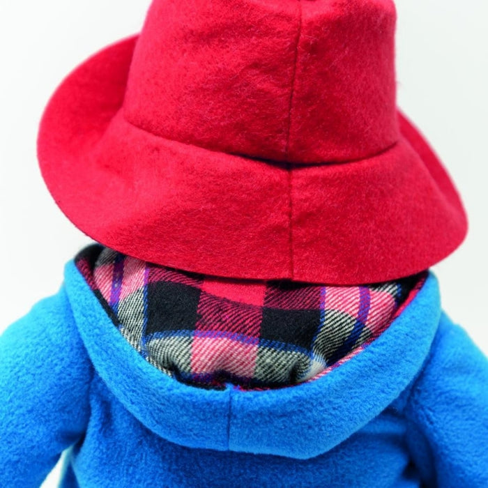 Close-up back shot of Paddington bear wearing a red hat and blue coat with plaid lining.
