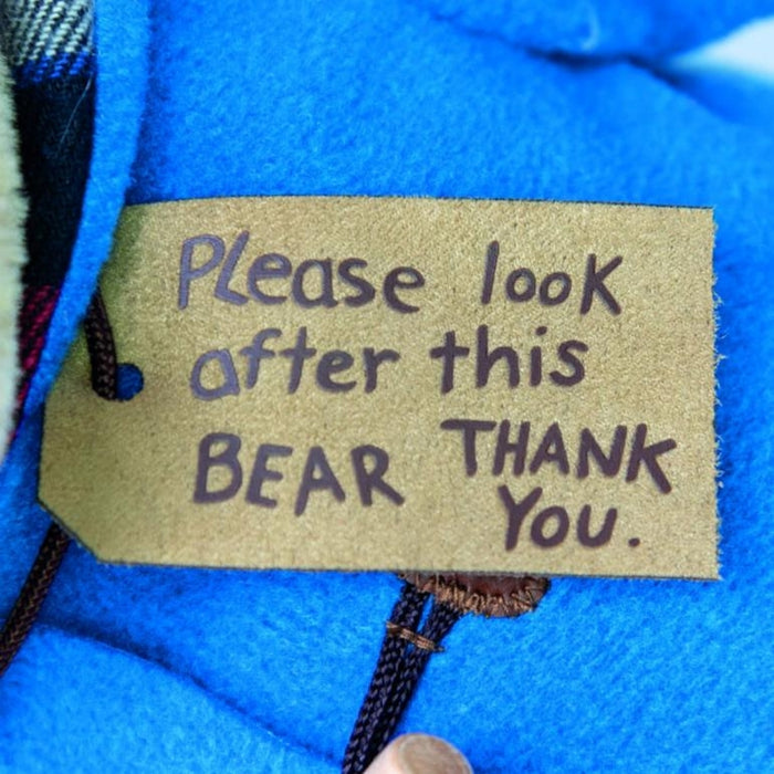 Textile luggae tag on a blue fabric background with 'Please look after this BEAR THANK YOU.' text.