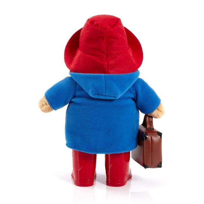 A Paddington plush toy figure shown from the back, wearing a red hat, blue coat, red boots, and holding a small brown suitcase against a plain white background.