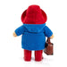 A Paddington plush toy figure shown from the back, wearing a red hat, blue coat, red boots, and holding a small brown suitcase against a plain white background.