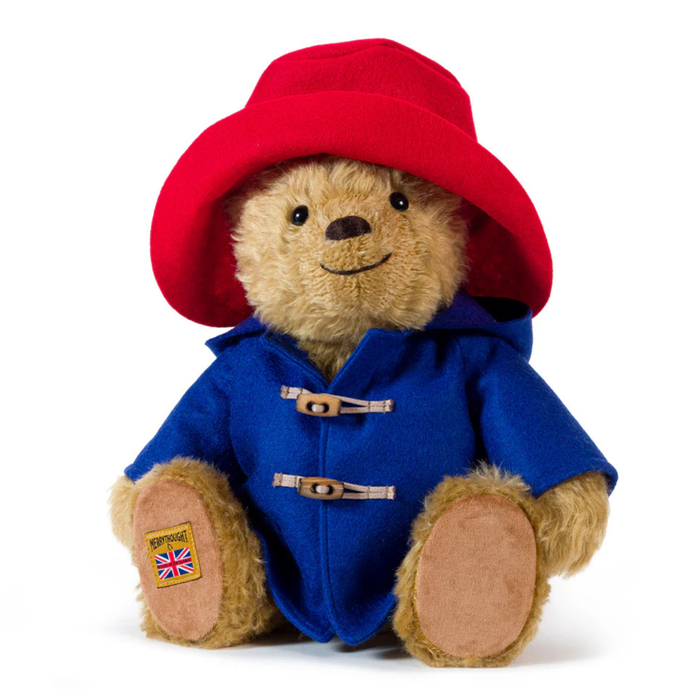 A Merrythought collectors Paddington teddy Bear plush toy wearing a red hat and blue duffle coat with toggle closures, photographed on a clean white background.