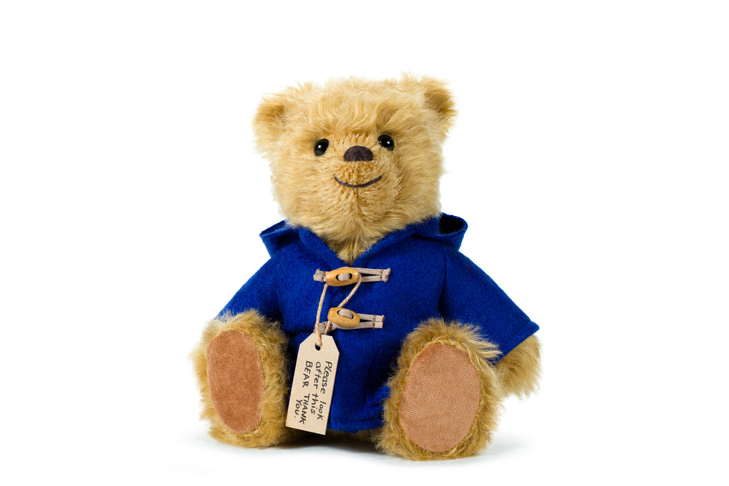 Paddington Teddy bear wearing a blue duffle coat with a white background