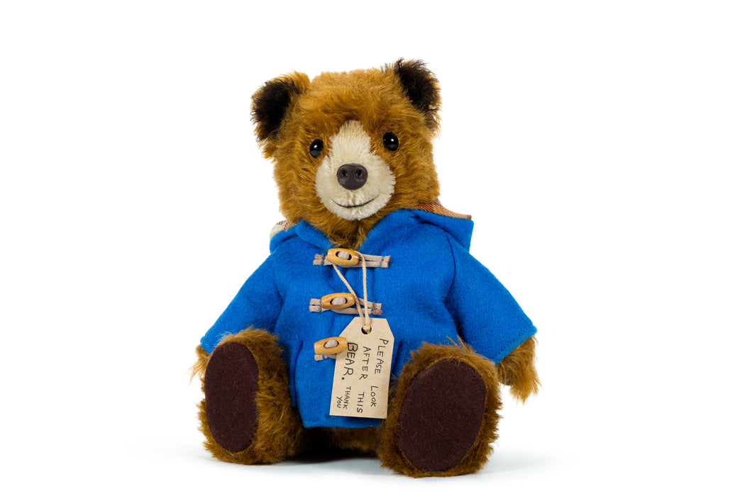 Stuffed paddington teddy bear wearing a blue coat with a tag on a white background