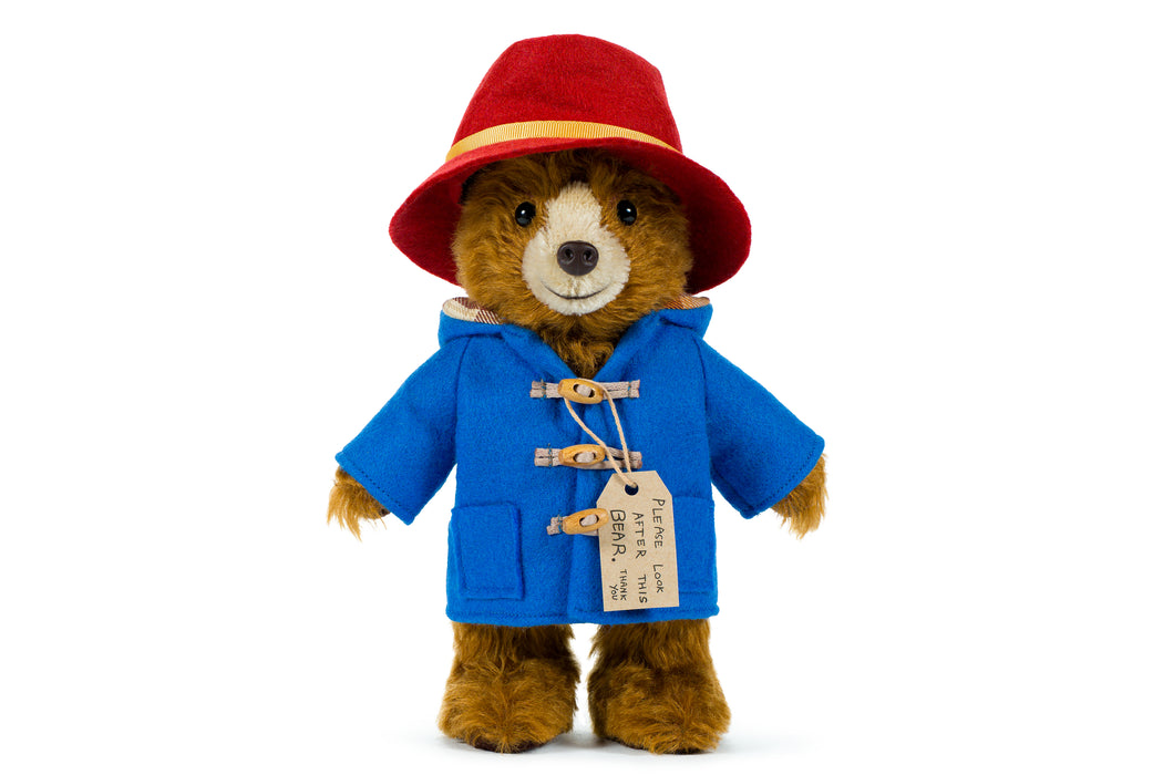 Stuffed toy paddington teddy bear in a blue coat and red hat on a white background