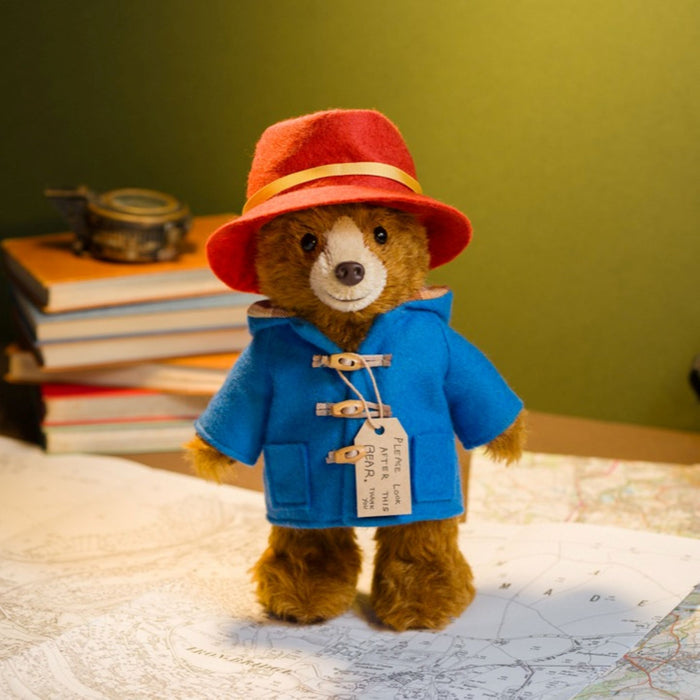 Stuffed Paddington teddy bear in a blue coat and red hat on a map with books in the background