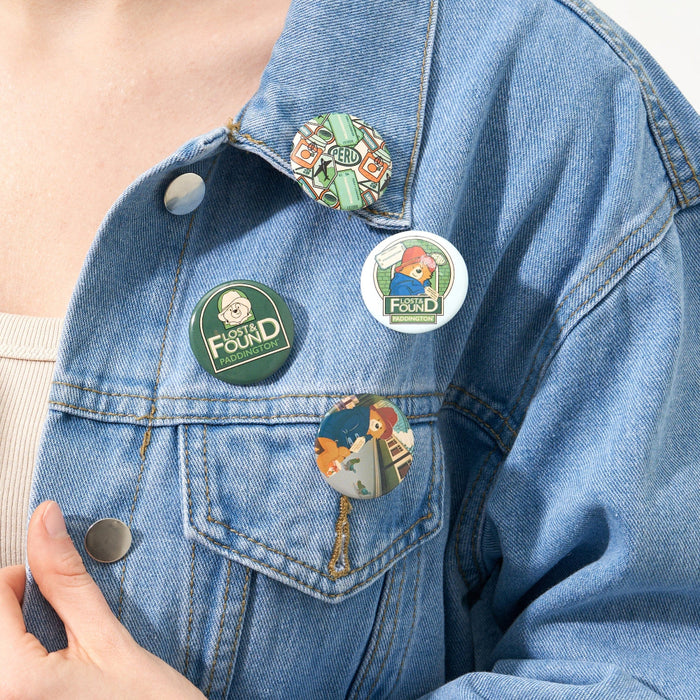 A set of four round badges with Paddington Bear designs affixed to a denim jacket.
