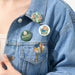 A set of four round badges with Paddington Bear designs affixed to a denim jacket.