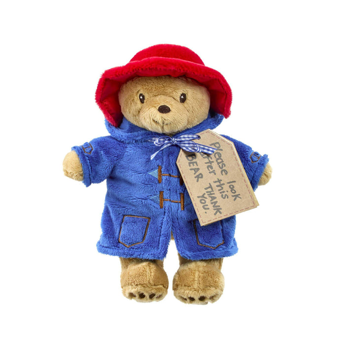 Plush toy Paddington bear in a blue coat and red hat with a tag on a white background