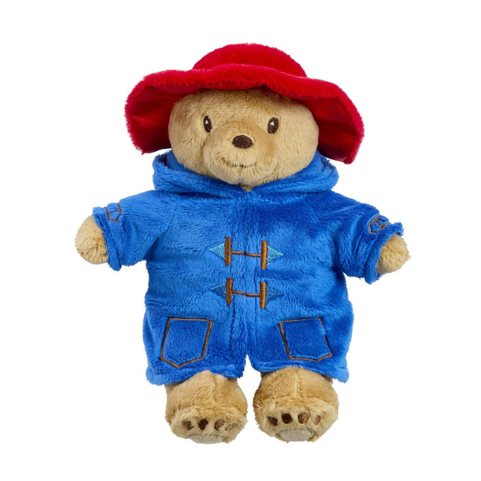 Stuffed toy Paddington bear wearing a blue outfit and red hat on a white background