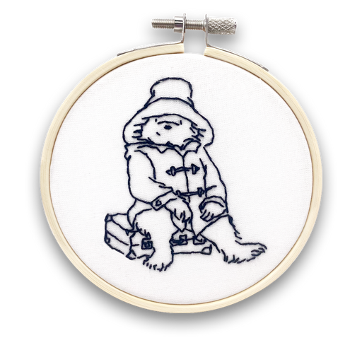 A mini embroidery kit depicting the character Paddington Bear sitting and appear to be enjoying a sandwich.