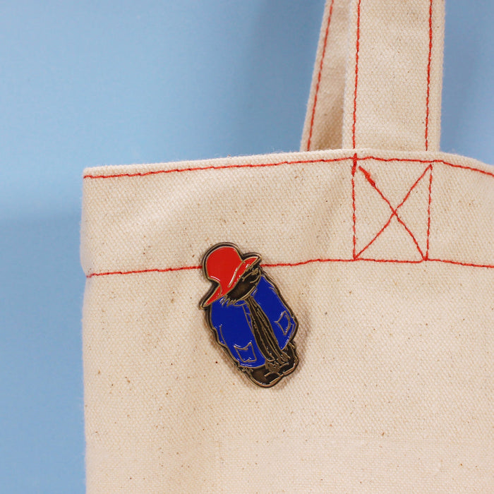 Pin of paddington bear wearing a red cap and blue coat on a beige fabric background