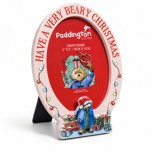 A decorative oval photo frame with a pink border and red center, featuring Paddington-themed Christmas artwork and the text 'HAVE A VERY BEARY CHRISTMAS' around the top. The frame is shown standing on a black easel against a white background.