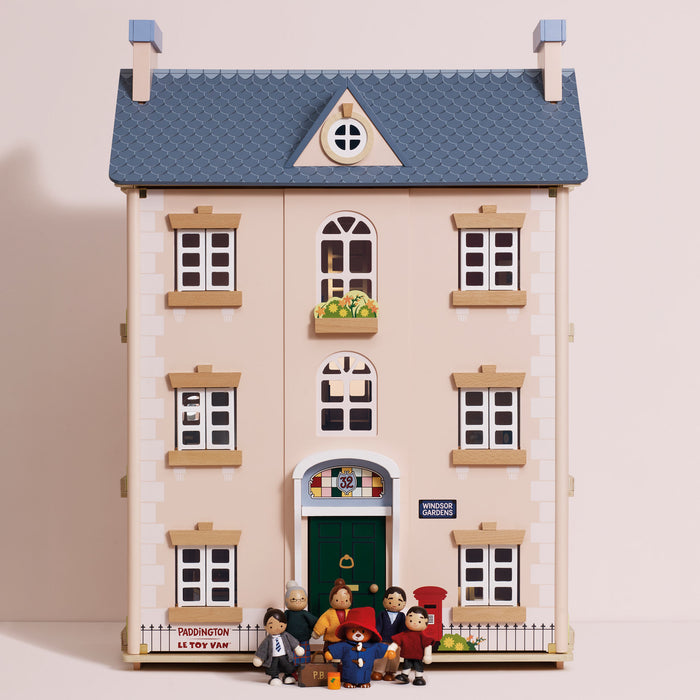 A miniature dollhouse of the iconic Paddington Bear house, featuring a beige facade, blue textured roof, green front door, and several small Paddington character figurines standing on the front porch.