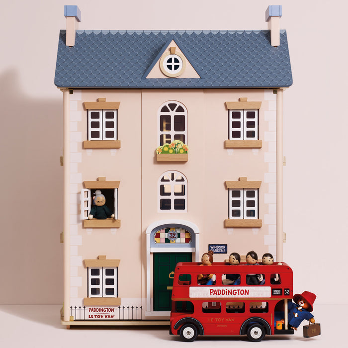 A toy model of Paddington's house with a red double-decker bus in front, featuring small figurines and detailed architectural elements on a plain beige background.