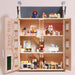 A miniature dollhouse with three open floors, furnished with tiny rooms, stairs, beds, tables, and small figurines, photographed against a plain light beige background.
