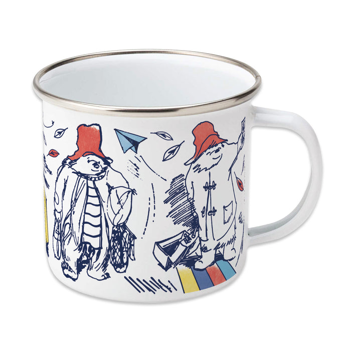 A white enamel mug with a handle on the right side, featuring colorful illustrations of Paddington Bear and other characters.