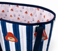 A corner shot of a navy blue and white striped quilted Paddington beach bag with Paddington bear face logo embroidery, navy blue handles and Paddingonton-esque printed lining.
