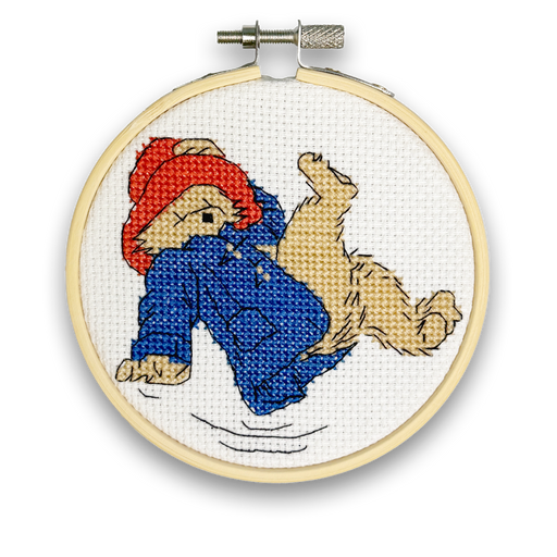 A mini cross stitch kit featuring an image of Paddington Bear wearing a blue outfit, falling over, with a white background.