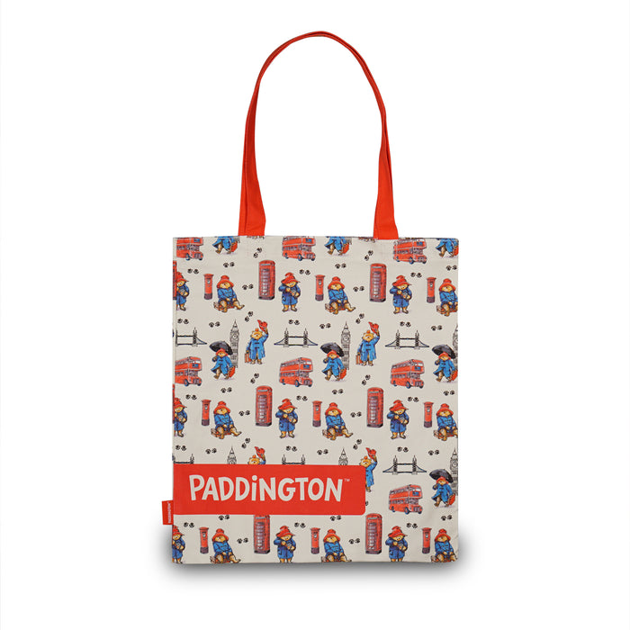 A canvas tote bag featuring a repeating Paddington Bear pattern on a cream background, with bright red handles and a red band at the bottom displaying the word 'PADDINGTON' in white text.