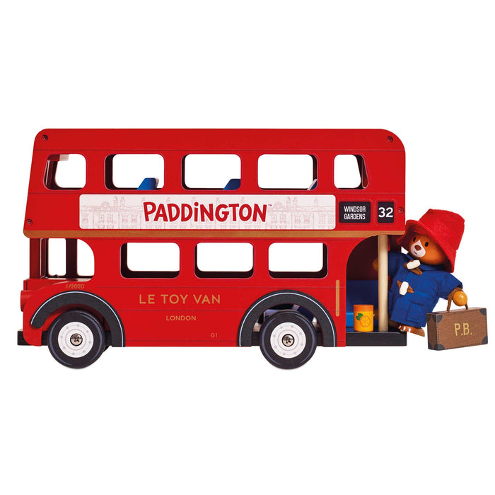 A red wooden double-decker bus toy with Paddington Bear character details, including a figure of Paddington standing at the open back door holding a suitcase.