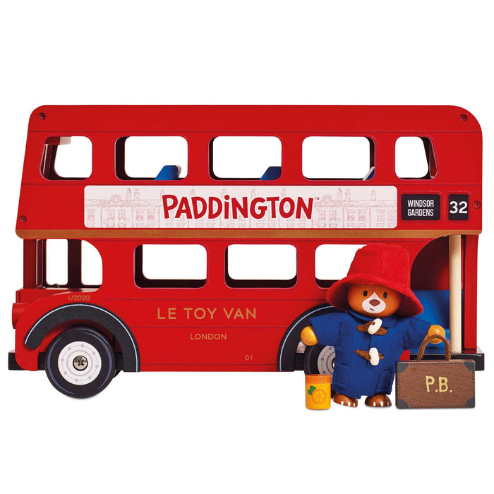 A red double-decker toy bus with Paddington Bear printed on the side, shown on a plain white background. The toy bus includes a small Paddington figure and suitcase at the front.