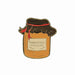 A pin badge featuring a jar of Paddington Marmalade with a label and a red ribbon on top.