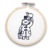 A mini embroidery kit depicting the character Paddington Bear holding a hat and a jar of marmalade, working on a piece of fabric.