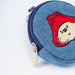 A close-up of a round blue denim coin purse featuring an embroidered Paddington bear character with a red hat and cream face, shown on a white background.