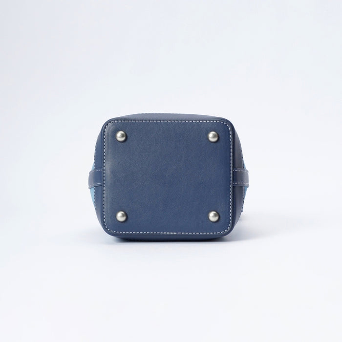 The bottom corner of a navy blue leather bucket bag, showing a square-shaped base with white stitching and four silver metal studs, on a white background.