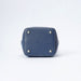 The bottom corner of a navy blue leather bucket bag, showing a square-shaped base with white stitching and four silver metal studs, on a white background.