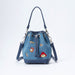 A blue denim bucket bag with dark blue leather trim, featuring embroidered Paddington bear patches and a drawstring closure, shown on a light grey background.