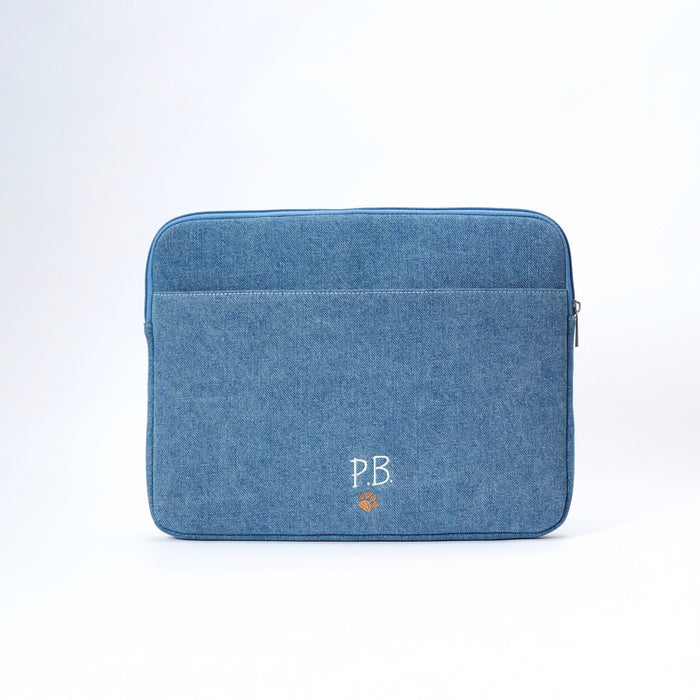 A blue denim laptop sleeve with a front pocket, featuring a white embroidered 'PB' logo and a small orange pawprint below it, set against a plain white background.