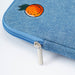 Close-up of a blue denim zippered laptop case featuring an embroidered orange with green leaves on the top corner and a silver metal zipper pull, set against a plain white background.