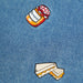 Close-up of a blue denim fabric featuring two embroidered patches: a small jar labeled 'Marmalade' with a red-and-white checkered lid, and a sandwich with orange marmalade filling.