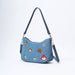 A blue denim shoulder bag with a dark blue leather strap and silver hardware, decorated with various colorful embroidered patches including an orange, a marmalade jar, and Paddington Bear.