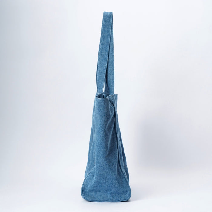 A blue denim canvas tote bag with a double shoulder strap, standing upright against a clean white studio background.