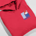 A folded red hoodie on a light gray background, featuring a cartoon illustration of Paddington Bear wearing a red hat and blue coat on the left chest, with the word 'PADDINGTON' printed below.
