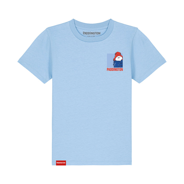 A light blue short-sleeve t-shirt featuring a small graphic of Paddington Bear on the left chest with the name 'PADDINGTON' printed below it. The brand name 'PADDINGTON' is also visible printed inside the collar and on a small red tag near the bottom hem.