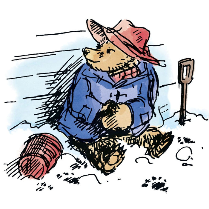 Illustration of Paddington bear character wearing a blue coat and red hat, sitting in the snow with a spade and ball of yarn.